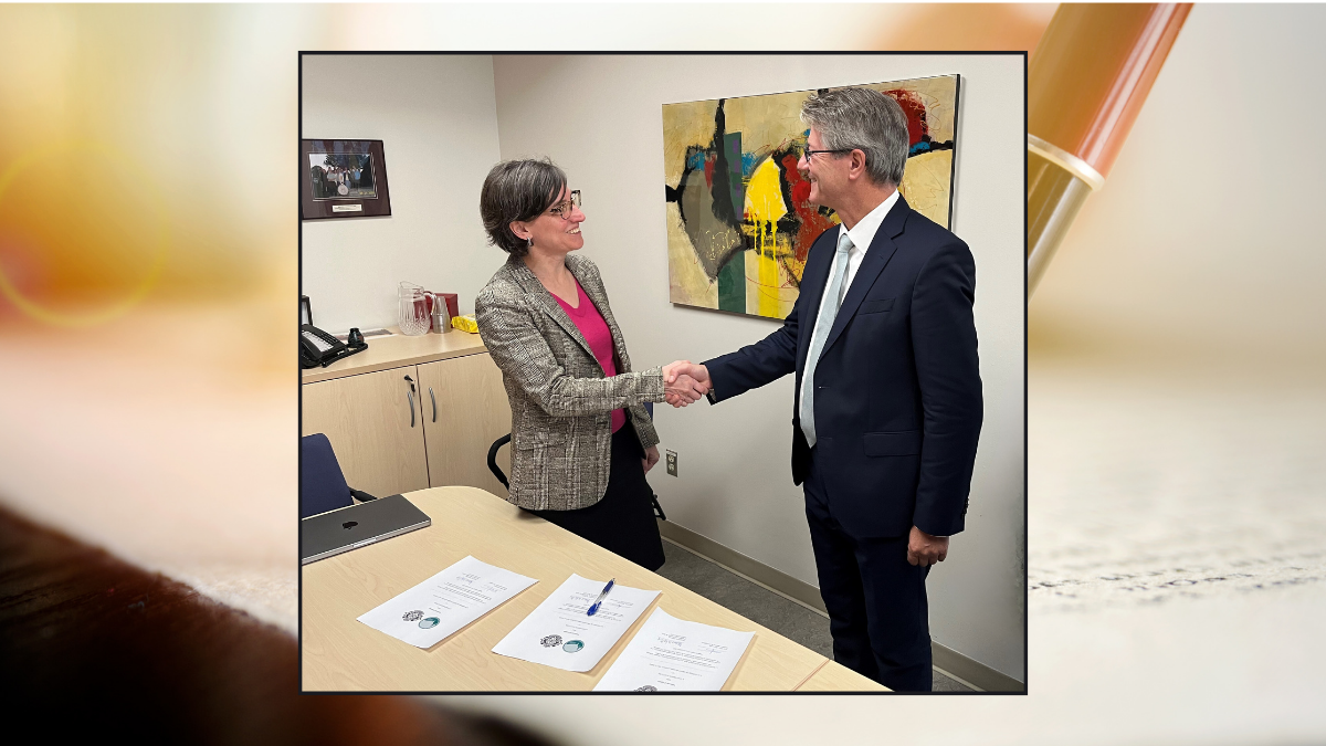 two people shake hands. there are papers and a pen on a table in front of them.