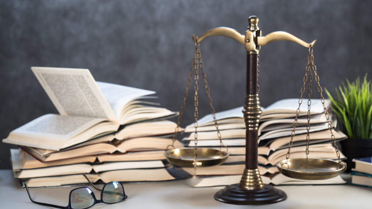 Deux piles de livres ouverts sont posées sur une surface, à côté d'une paire de lunettes et d'une balance.