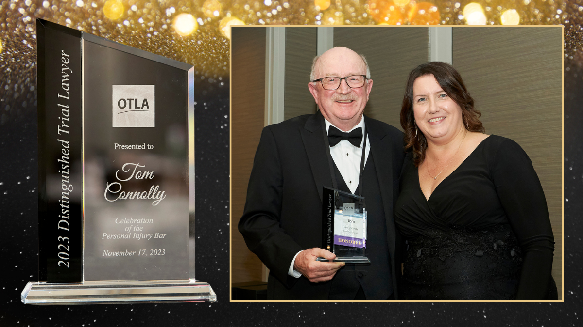 A man in a tuxedo stands with a woman in a black dress. He is holding a glass award in his hand. They are both smiling.