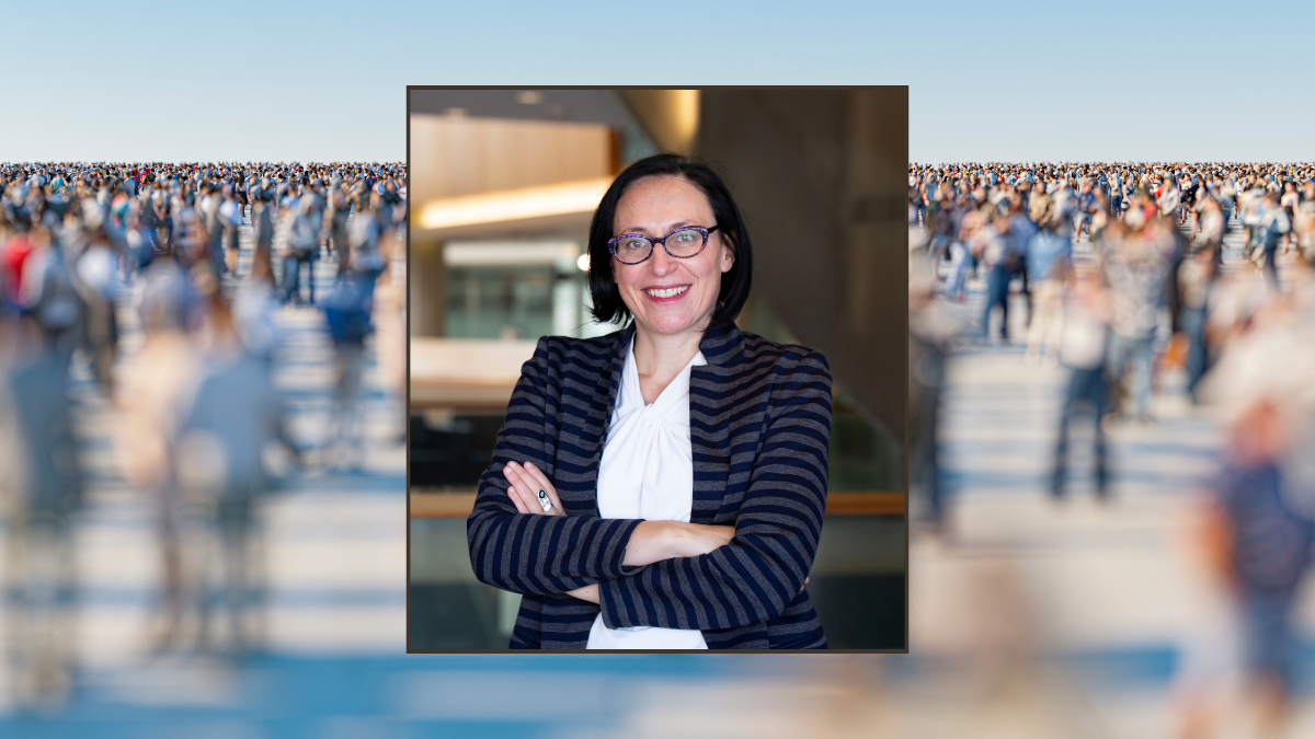 A photo of the professor Delphine Nakashe, smiling with arms crossed. The background photo is a crowd of people walking.
