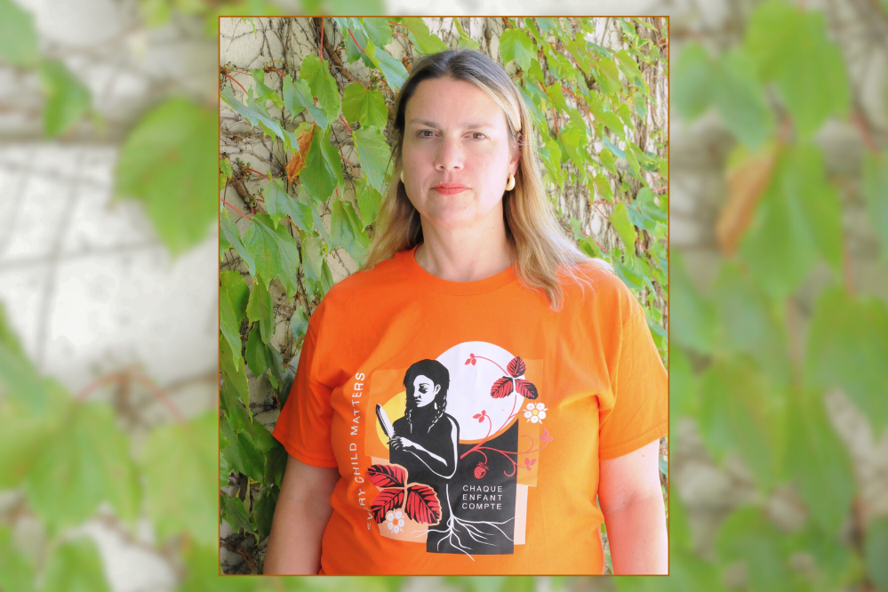 Kristen Boon wearing an orange shirt for National Day for Truth and Reconciliation. She is leaning against a wall that is covered in green leaves.