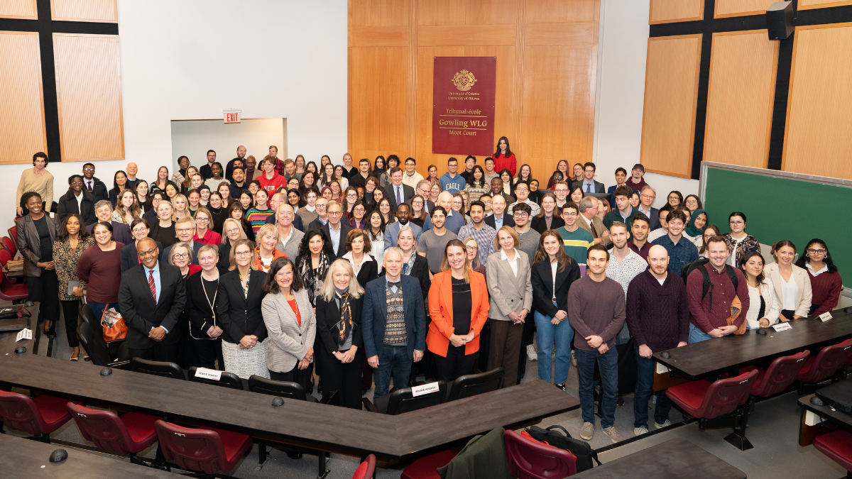 A large group of faculty members, students and judges from the Ontario Court of Appeal stand together, smiling, in a law school classroom