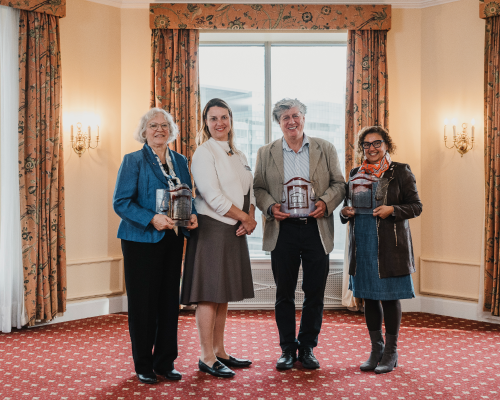 four people stand, shoulder-to-shoulder, smiling. Three are holding award.