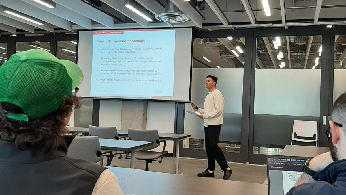A student stands at the front of the classroom. There is a presentation on a large screen beside him.
