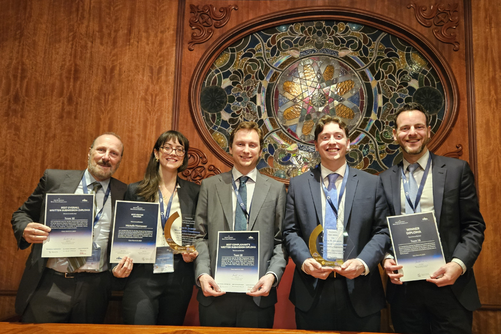 Five people, wearing suits and smiling, hold awards and certificates.