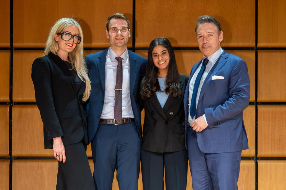 Four people in suits, stand smiling.