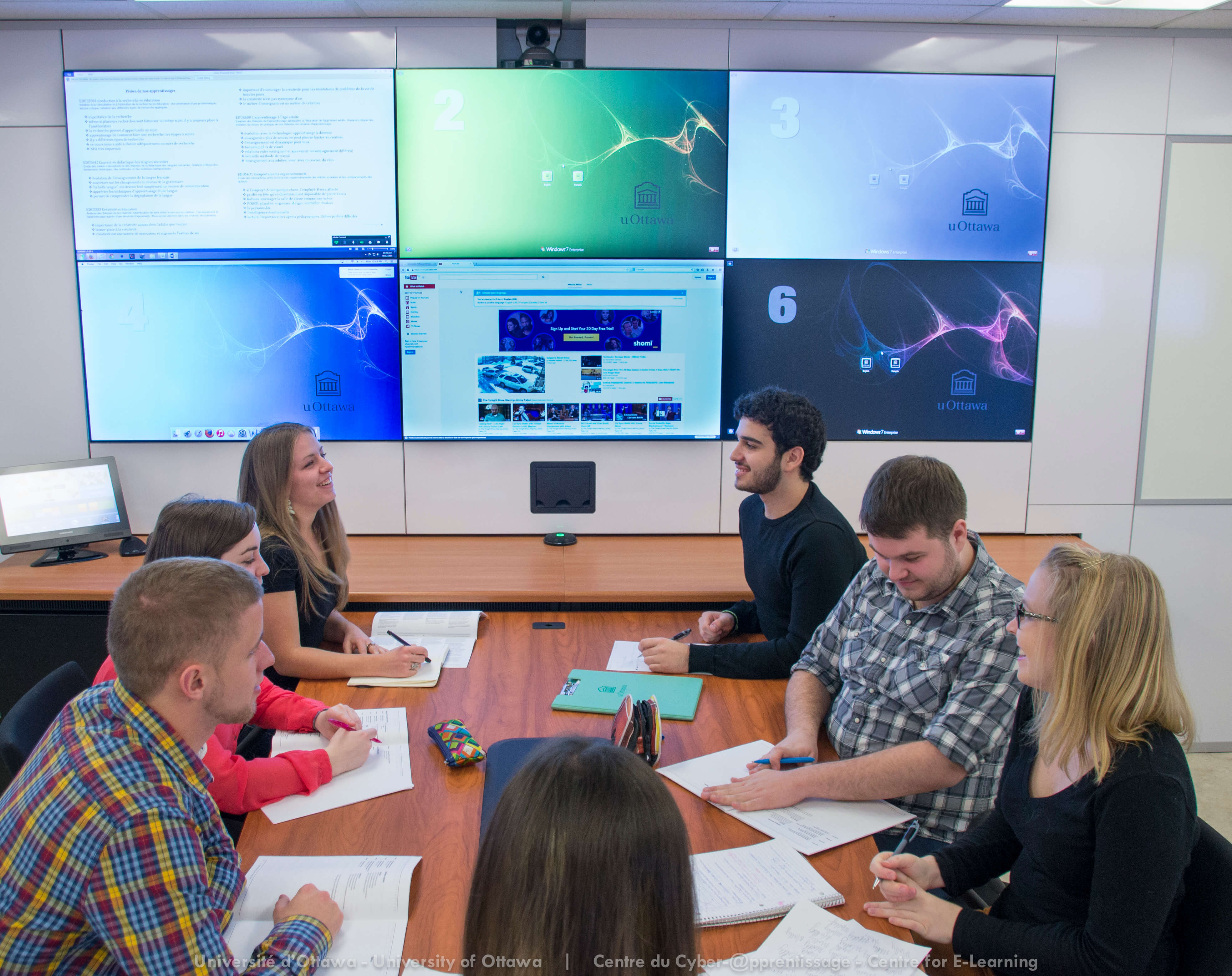 Un groupe d’étudiants assis autour d’une table de conférence, face à plusieurs écrans affichant diverses images scientifiques et présentations.