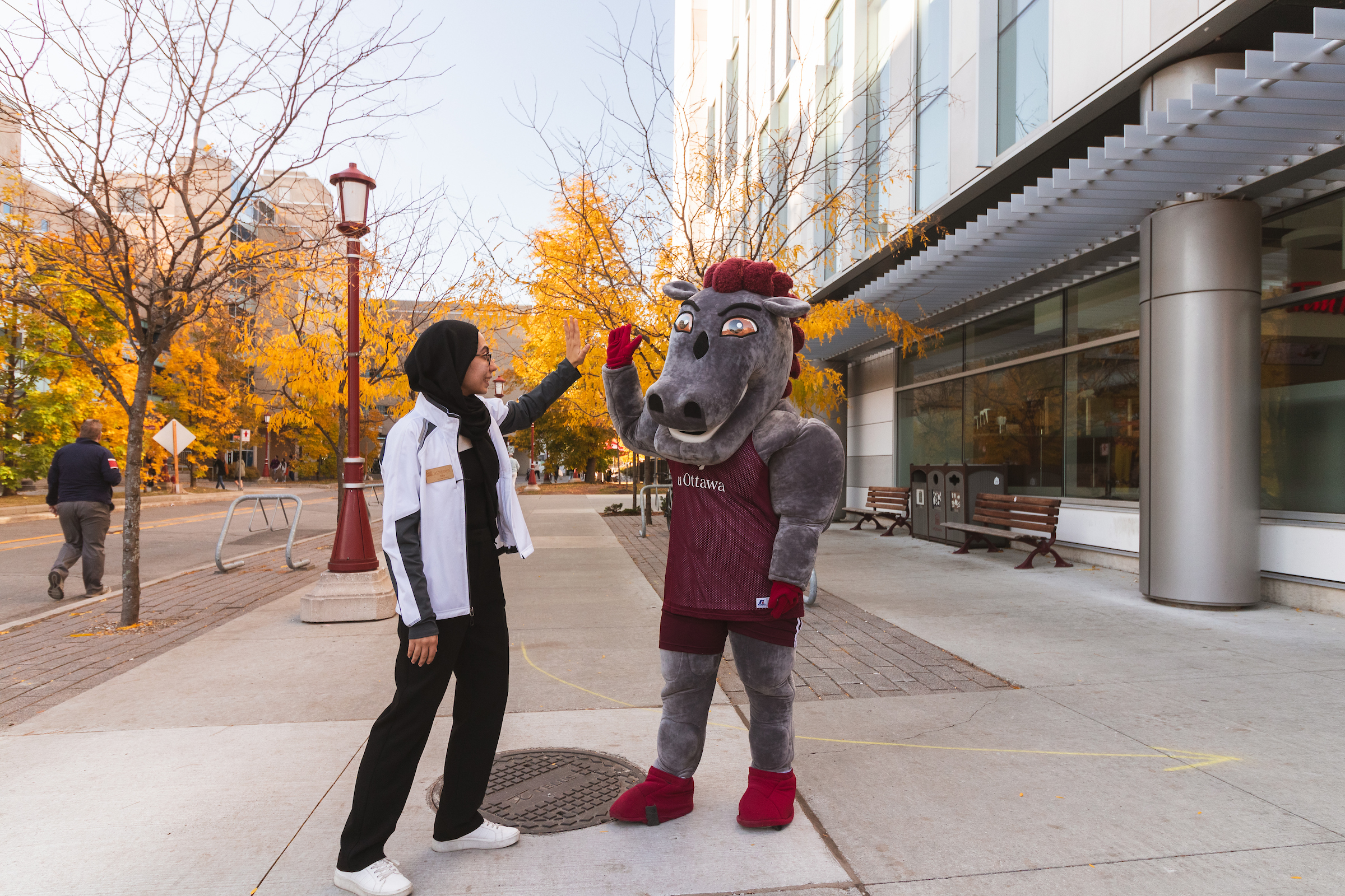 La mascotte des Gee-Gees donne un « high five » à un·e étudiant·e à l’extérieur.