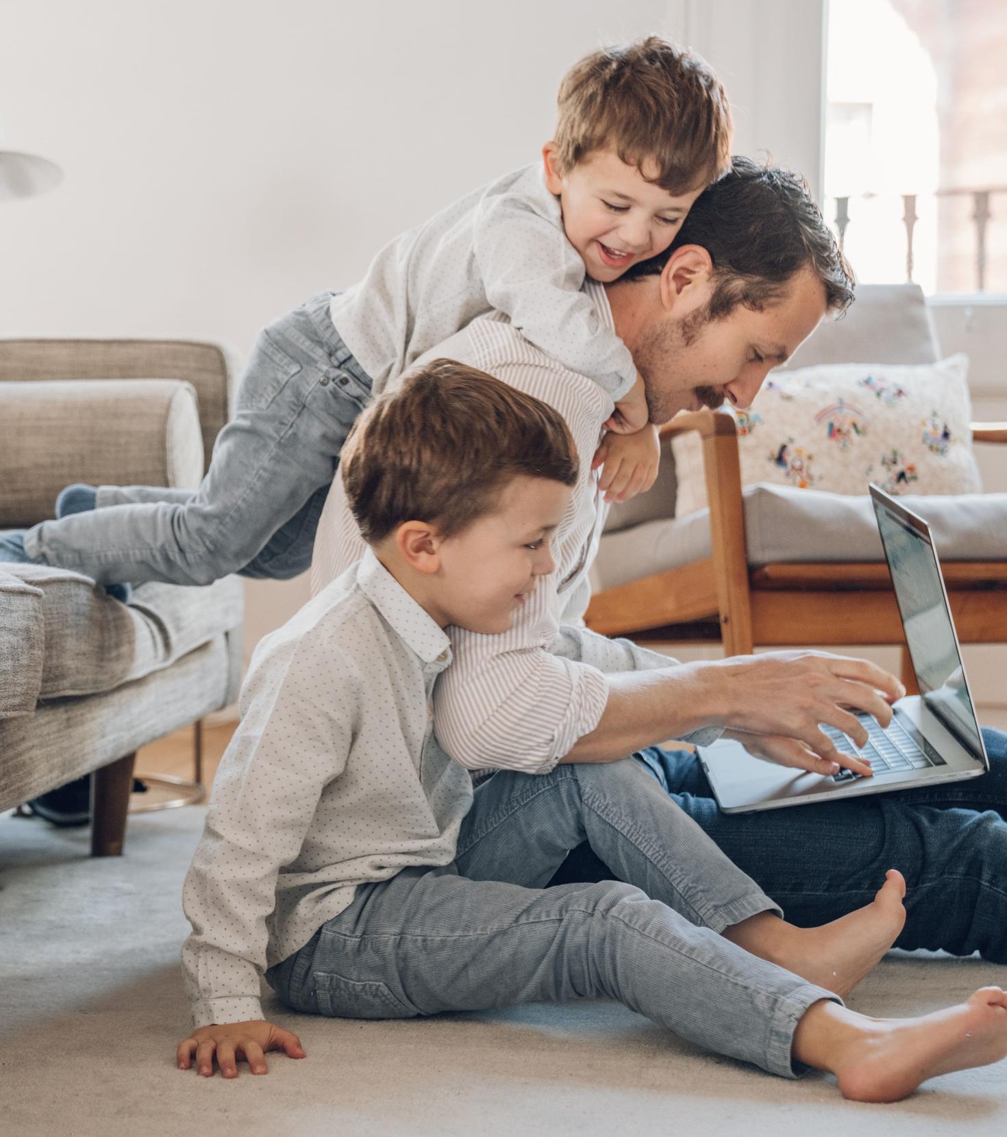 Père travaillant avec des enfants grimpant sur ses épaules.