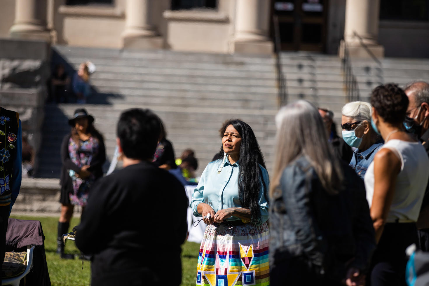 Groupe d'individus. La plupart sont flous mais une femme apparaît bien en vue au centre. Elle semble parler au groupe qui l'entoure.