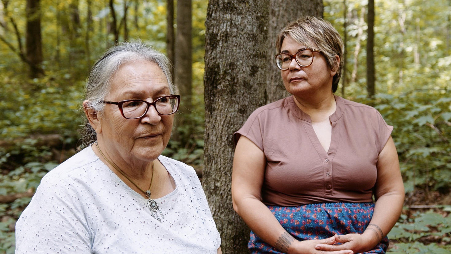 Mariette Niquay et Eva Ottawa sont assises sur une bûche dans le bois.