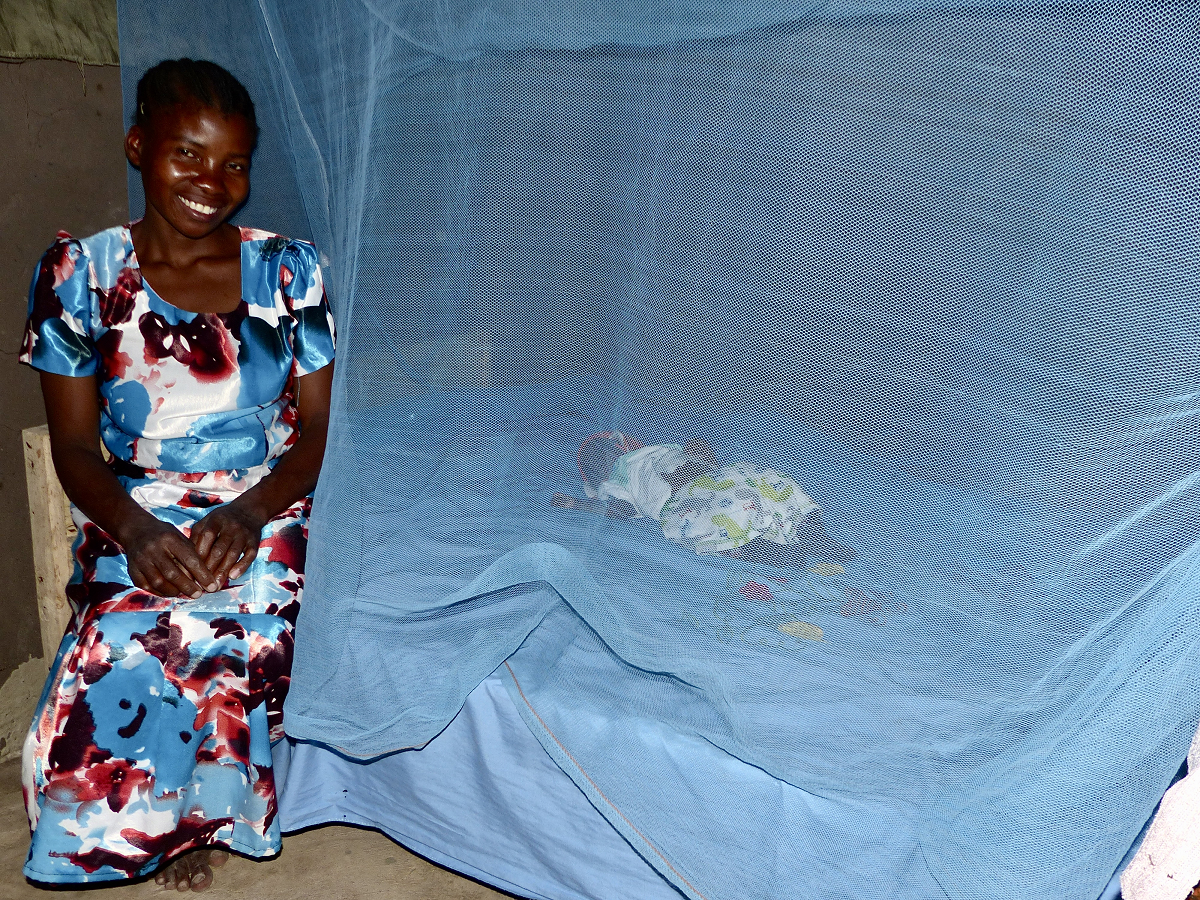 Femme africaine assise sur un lit où l'enfant dort dans un filet.