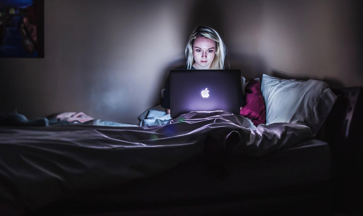 Femme regardant un ordinateur dans le noir, au lit