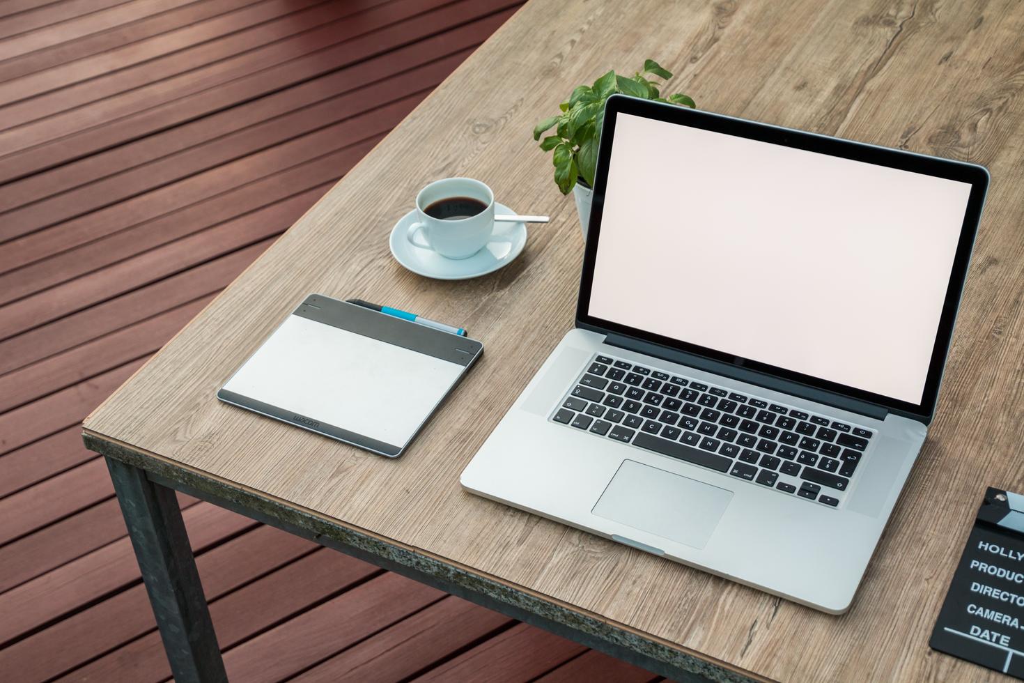 Bureau avec ordinateur portable, café, plante et cahier.