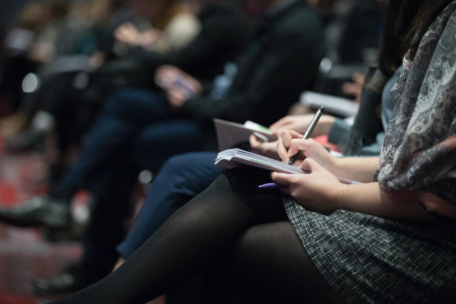 Les personnes en rang sont assises et écrivent dans des cahiers tout en écoutant une présentation
