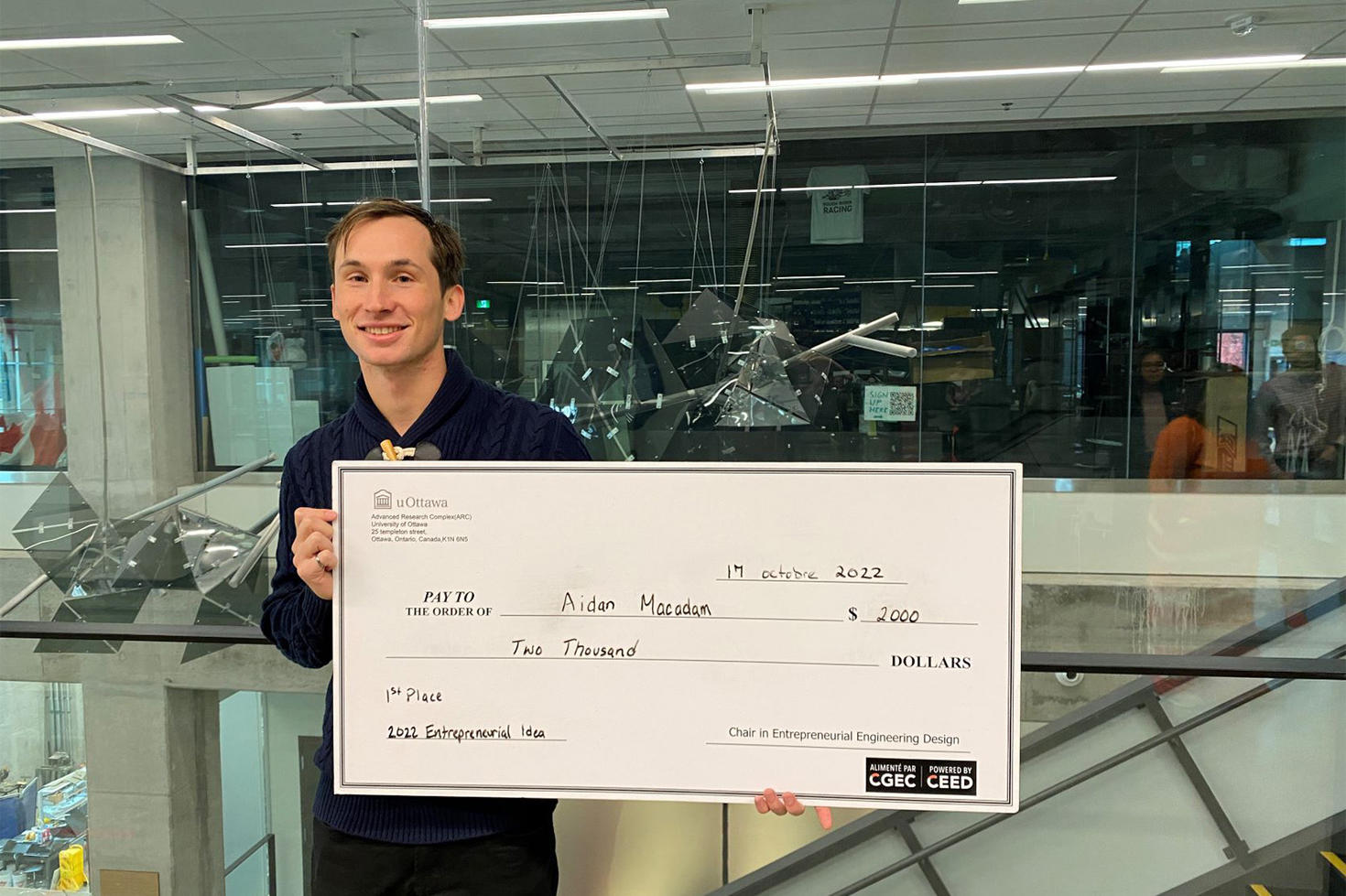 Aidan MacAdam tient dans ses mains un chèque géant d'une valeur de 2000 $.