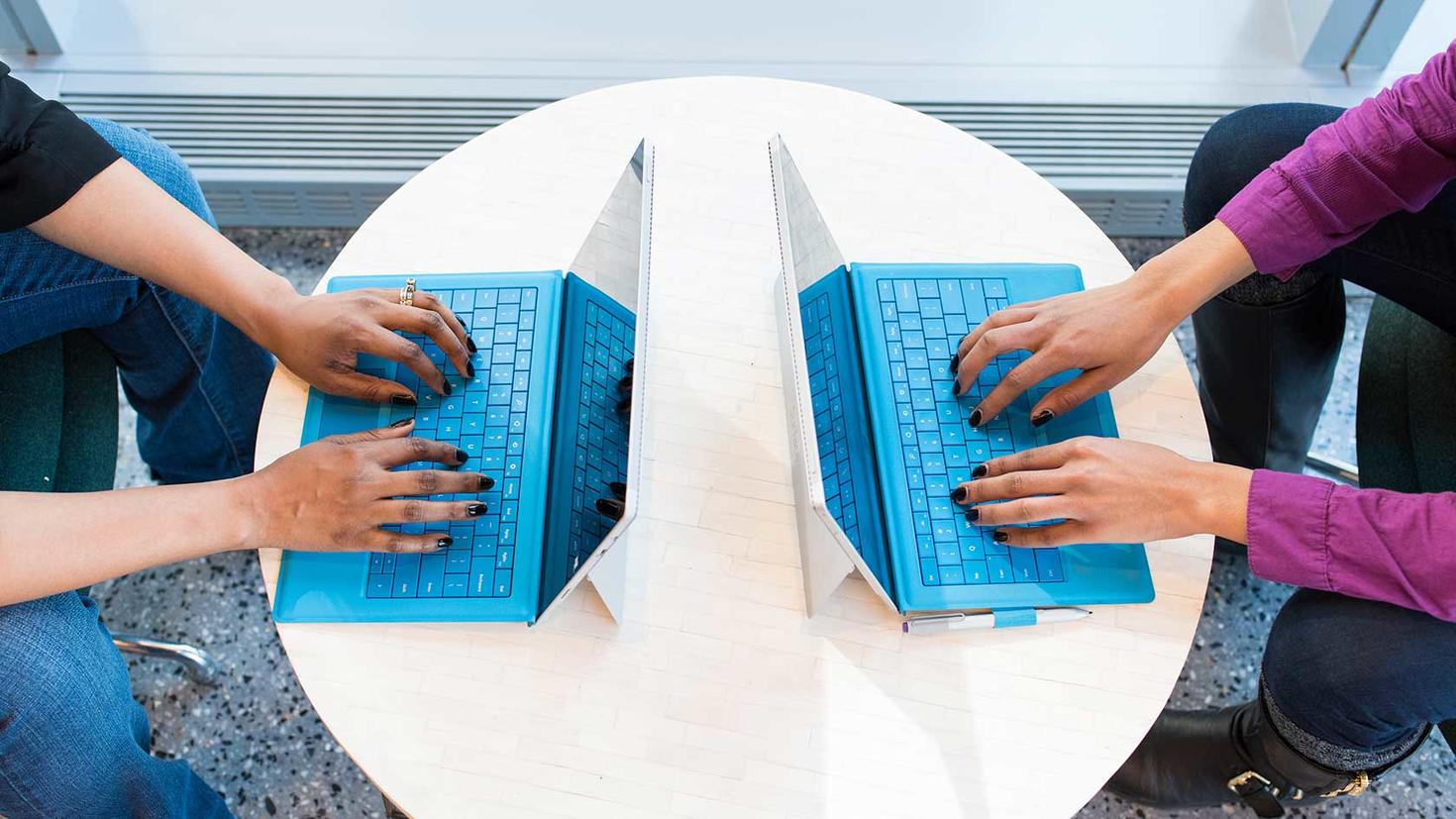 Deux personnes travaillant sur leur ordinateur portable, face à face sur une table basse.