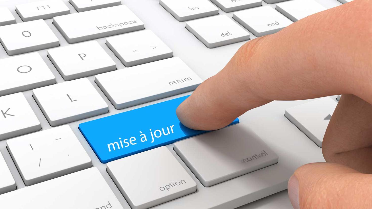 Clavier d'ordinateur avec une touche bleue "mises à jour" et un doigt survolant cette touche.