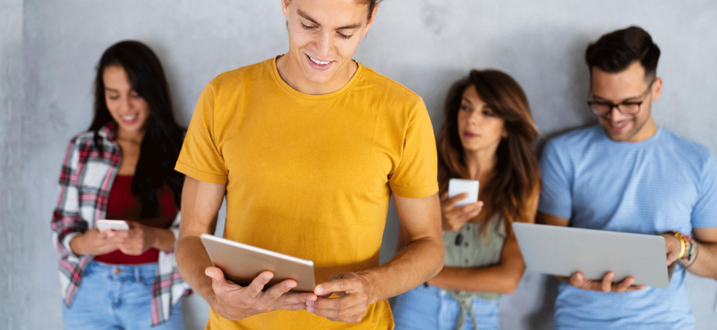 4 élèves debout devant un mur tenant différents appareils (smartphone, tablette, ordinateur portable)