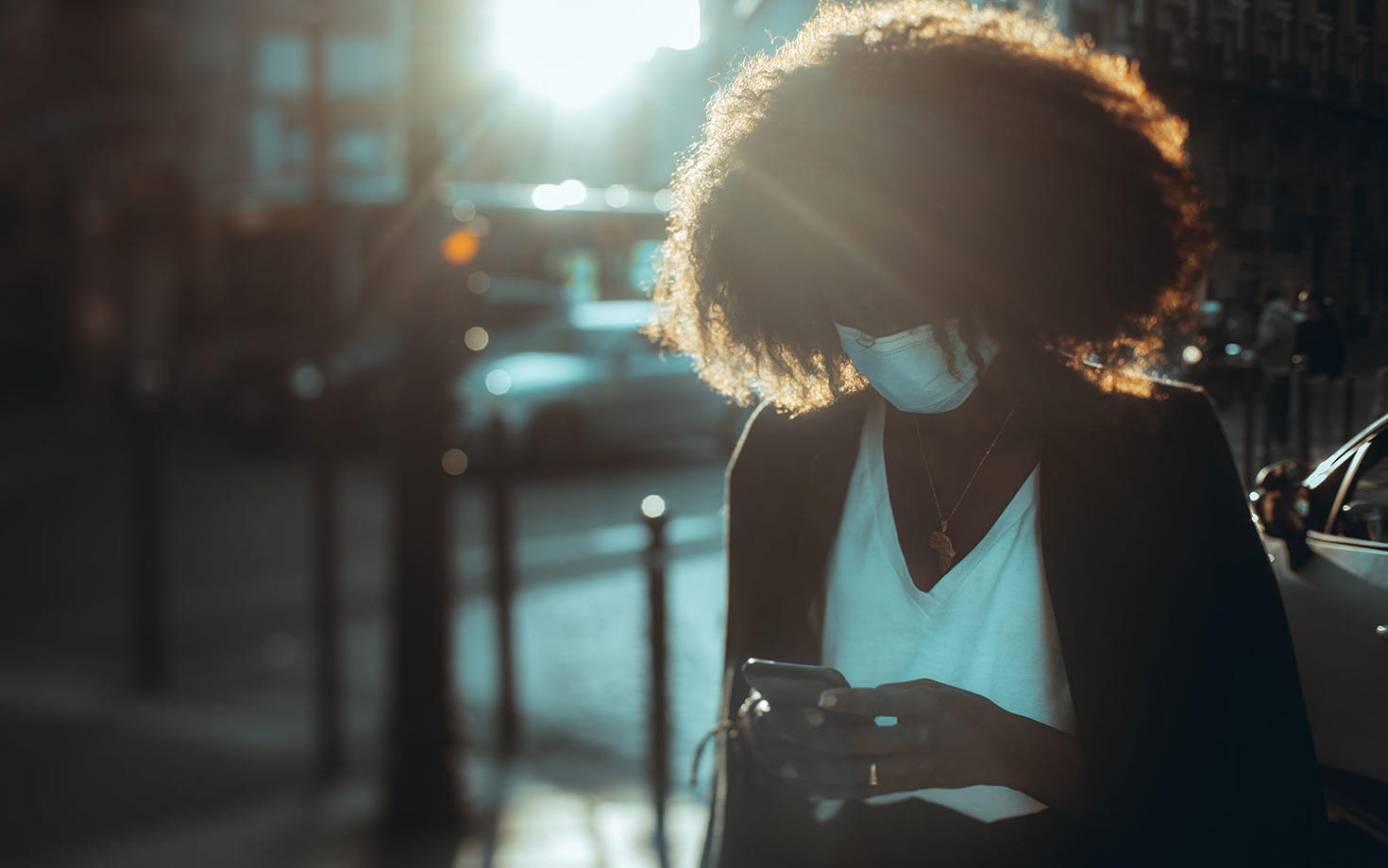 Une femme regarde son cellulaire et porte un masque.