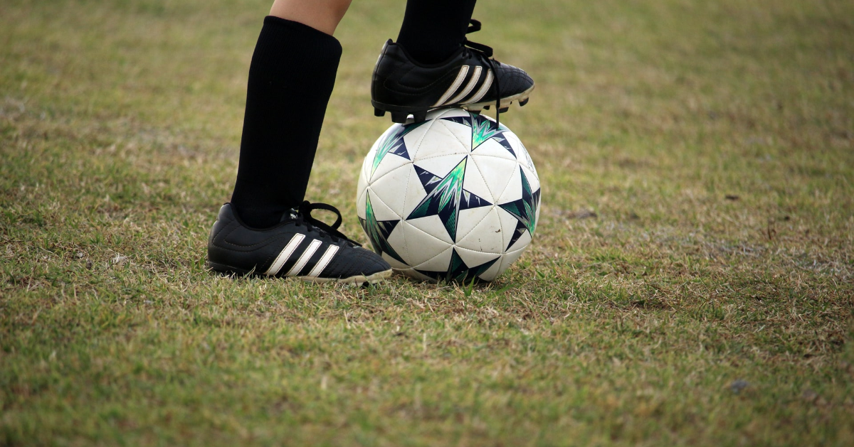 Pieds d'un enfant portant des crampons de football avec un pied sur le ballon de football.