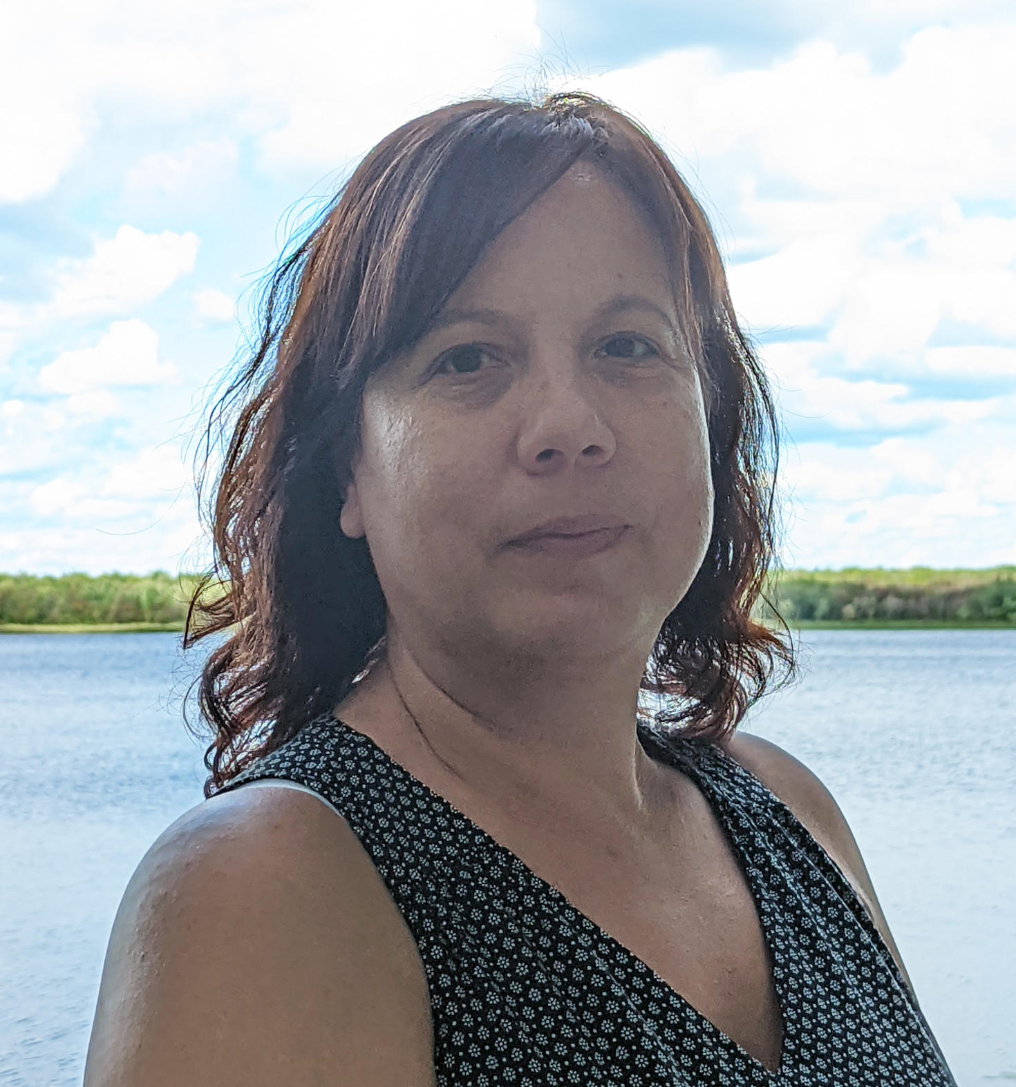 Photo of woman standing by water with blue sky and clouds in background