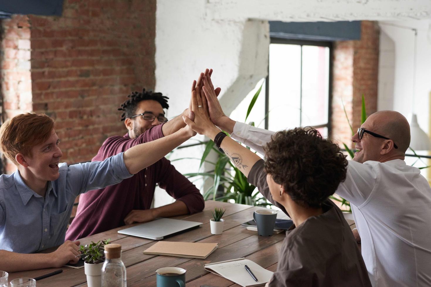 Groupe d'individus assis à une table et se donnant un "high-five" de groupe