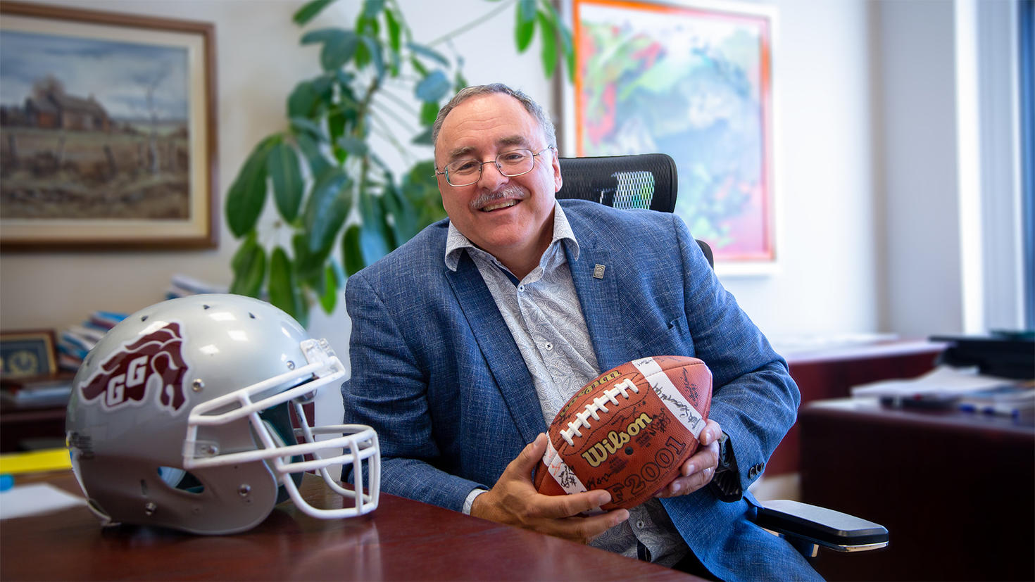 Sylvain Charbonneau dans son bureau, tenant un ballon de football signé par l'équipe des Gee-Gees