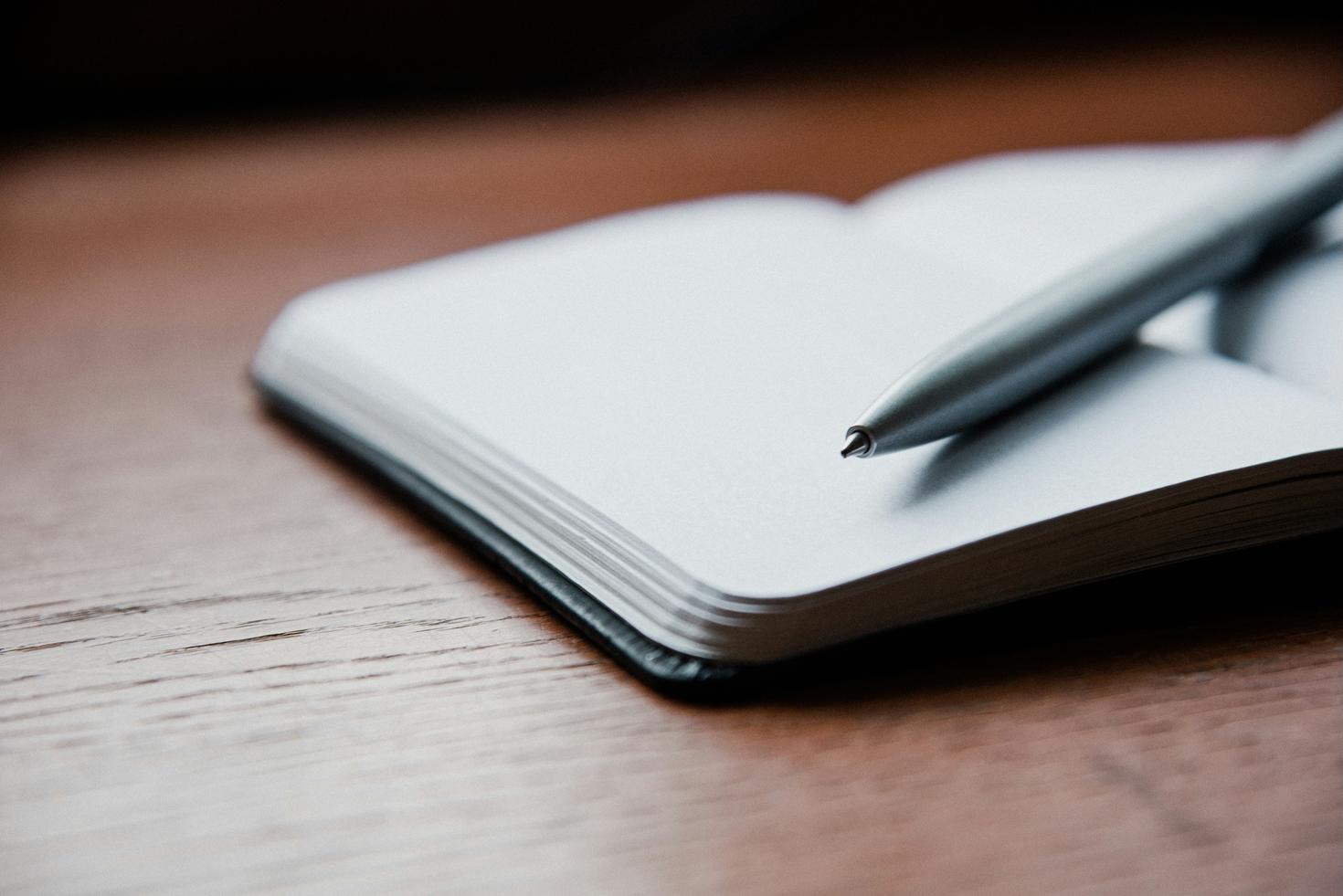 cahier de notes ouvert, déposé sur une table avec un crayons déposé sur les pages
