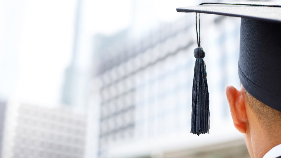 Arrière d'une tête portant une toque de graduation, face à un bâtiment flou