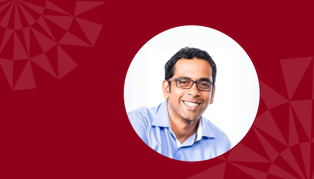 Portrait d’un employé de l’Université d’Ottawa, portant des lunettes et une chemise bleue à col, présenté dans un cercle blanc sur un fond rouge foncé aux motifs géométriques abstraits.