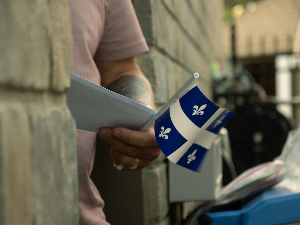 Un homme tenant un bulletin de vote et un drapeau du Québec