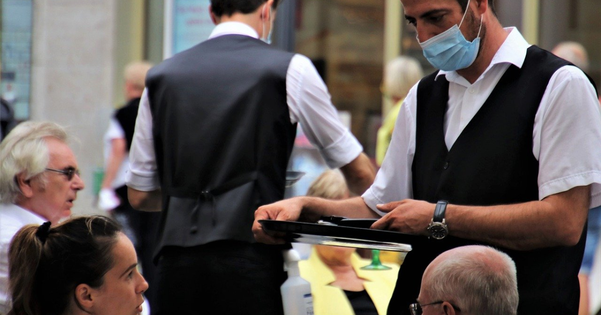Un serveur qui porte un masque et qui prend la commande de clients dans un restaurant