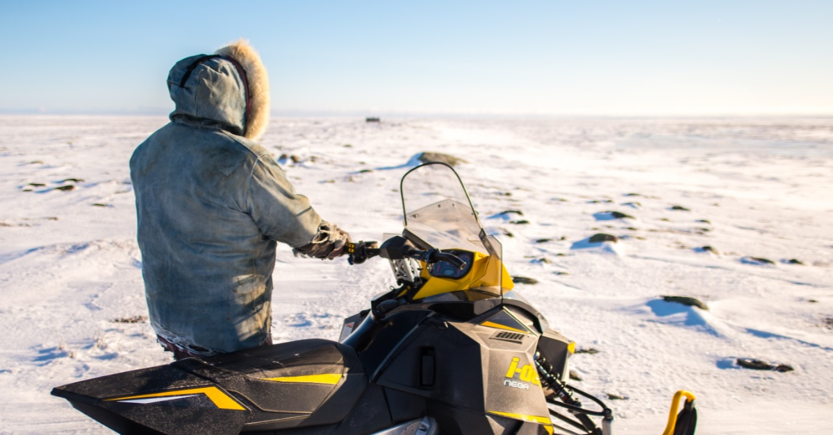 Un Inuit se tenant à côté de sa motoneige en Arctique