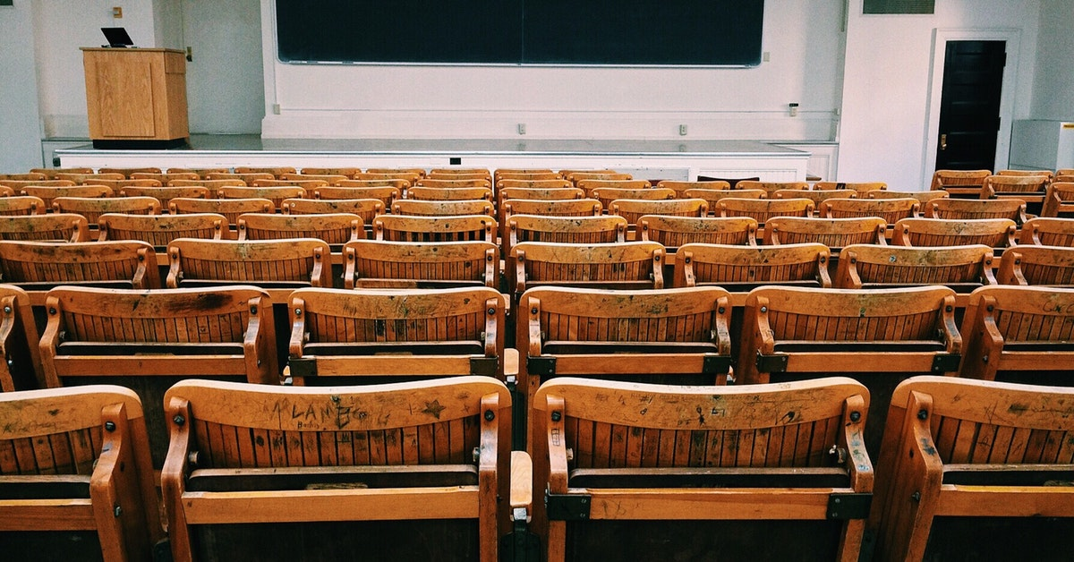 Des rangées de sièges inoccupés dans une salle de classe universitaire vide.