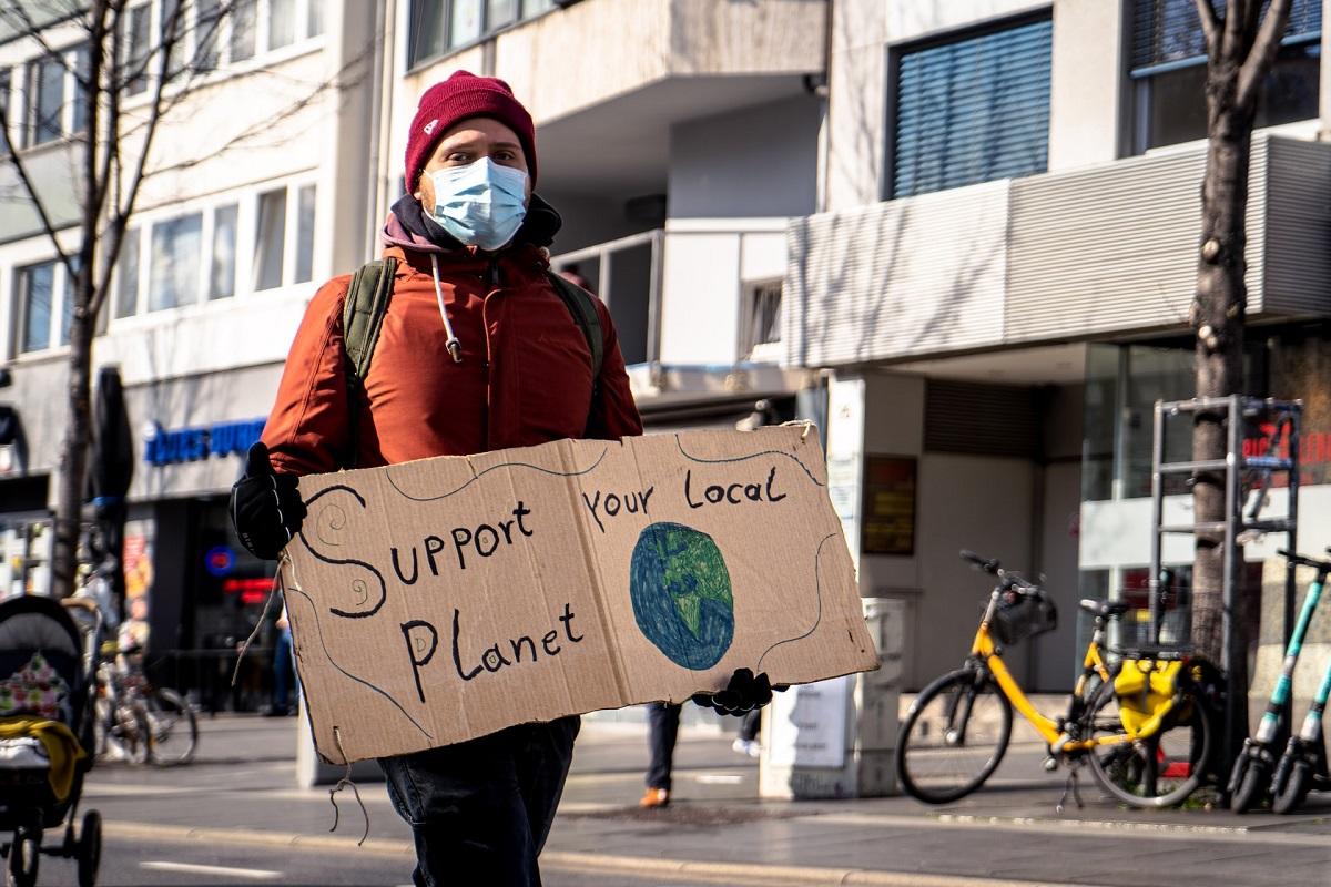 Un manifestant tient une pancarte indiquant « Support your local planet » avec le dessin d'un globe terrestre