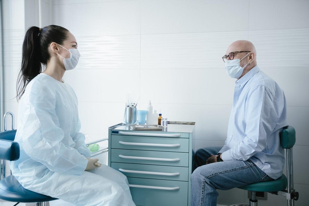 Un médecin parle avec un patient, tous deux portant des masques