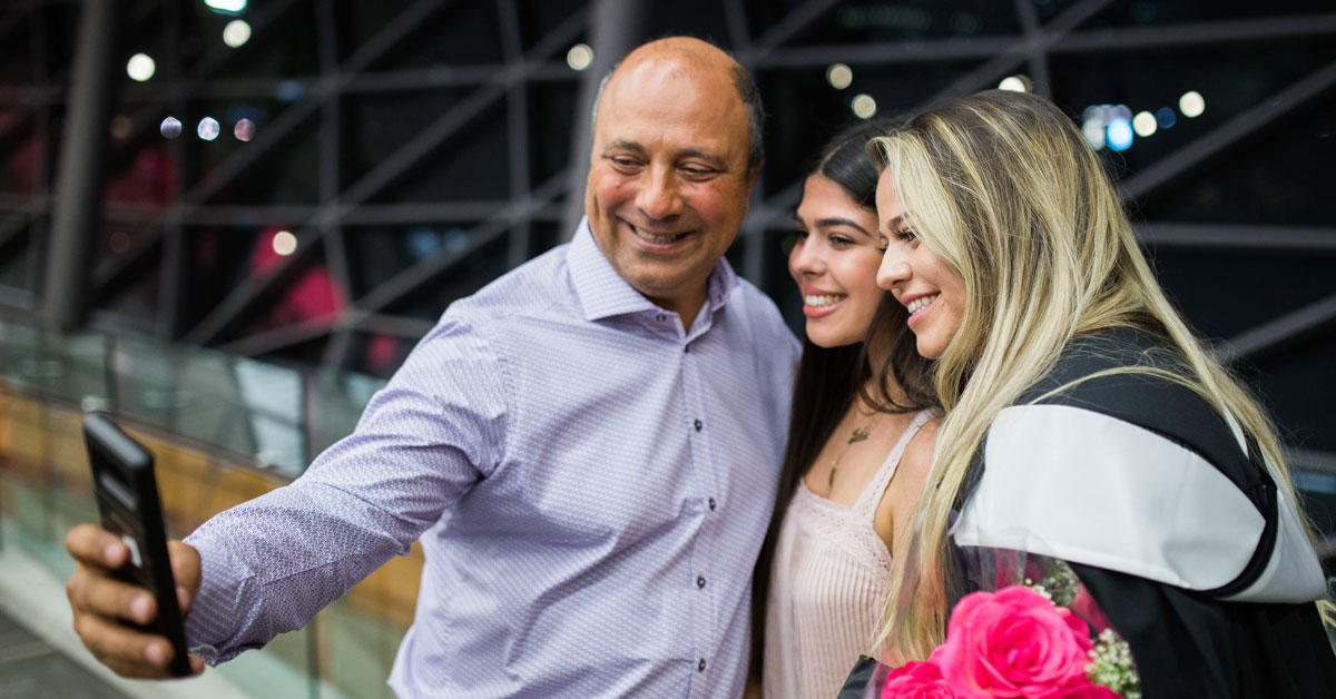 A father and his two daughters take a selfie at graduation.