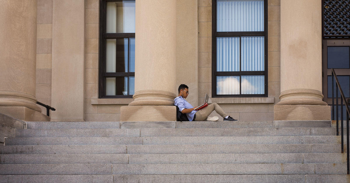 Student with his laptop sitting alone on the steps of Tabaret Hall