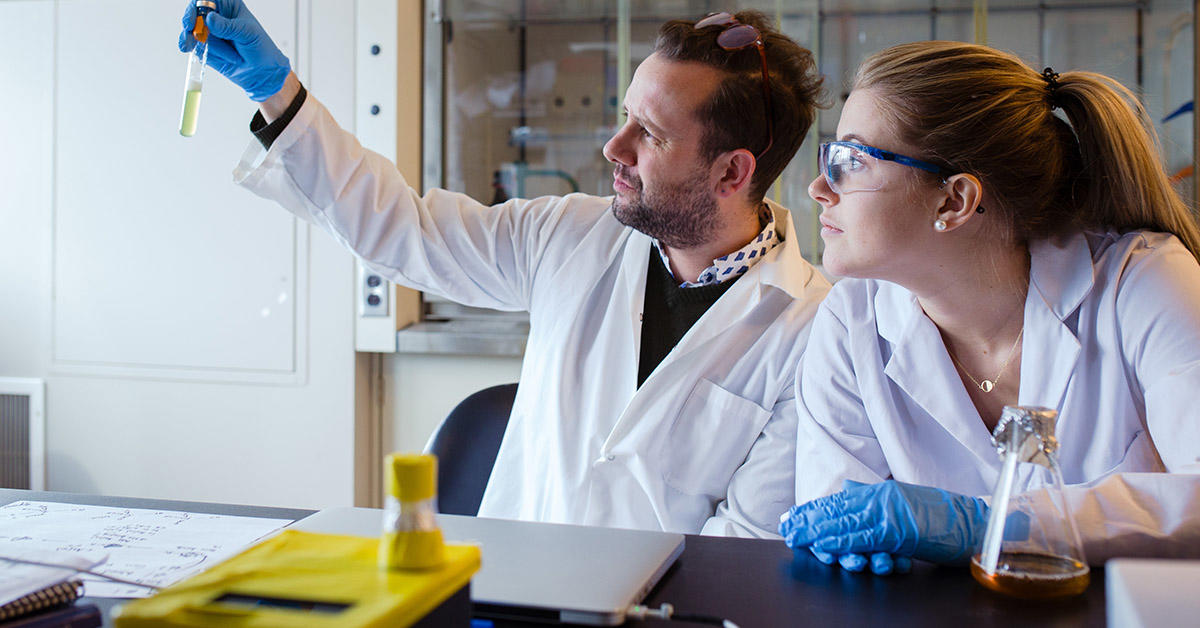 professor Alexandre Poulain looks at yellow yeast sample in test tube to verify clarity with Jessica Gaudet