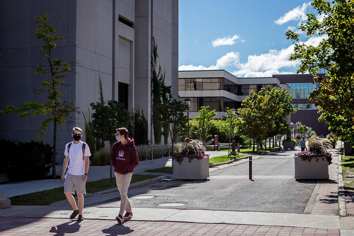 deux étudiants marchant sur le campus, portant des masques faciaux et socialement distants