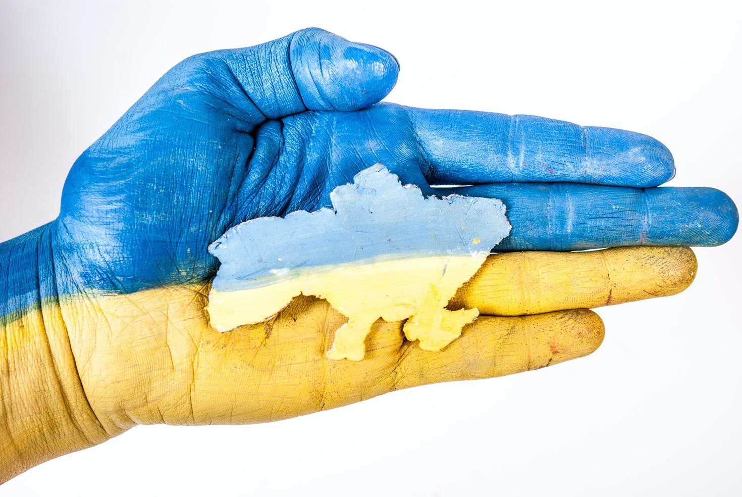 Hand holding cutout of Ukraine painted in colours of the flag