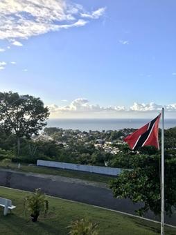 Drapeau de Trinité-et-Tobago sur le côté droit du premier plan. Une route sur le côté, le ciel et la mer en arrière-plan.