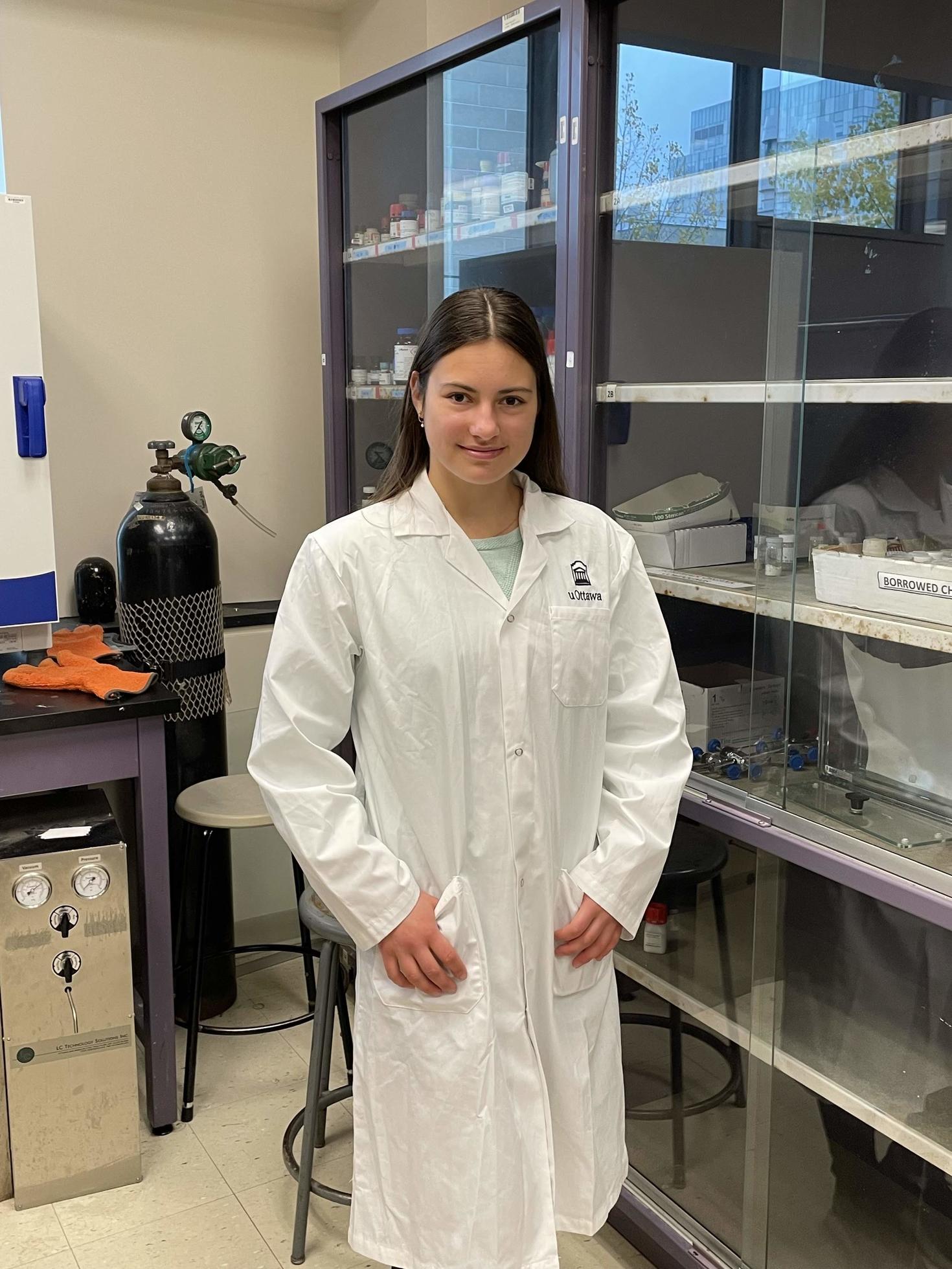 Mila debout dans un laboratoire, vêtue d'une blouse de laboratoire