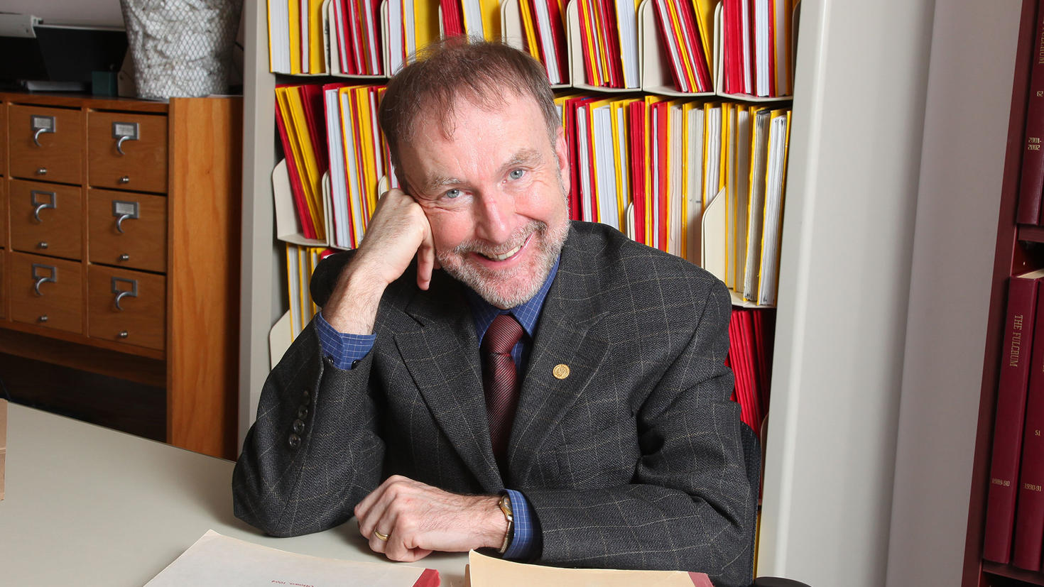 Michel Prévost sitting at his desk in front of a bookcase full of books.