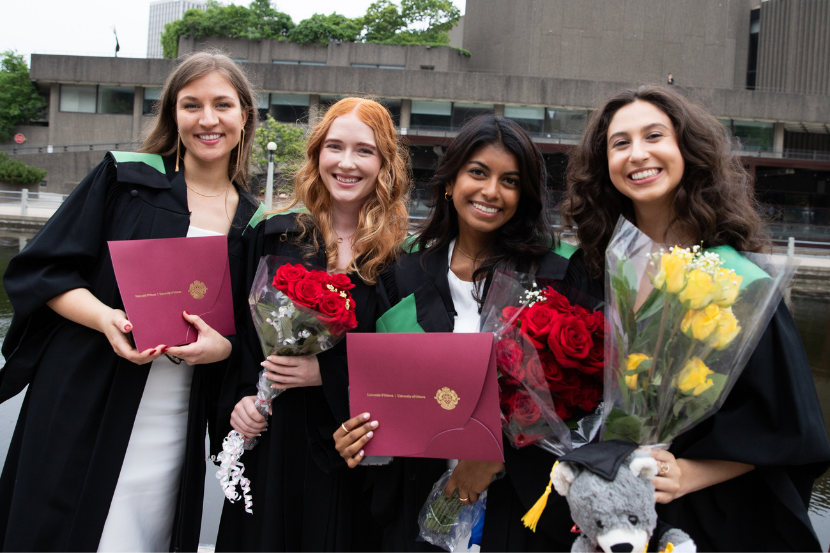 4 graduates with flowers and their diplomas after the ceremony