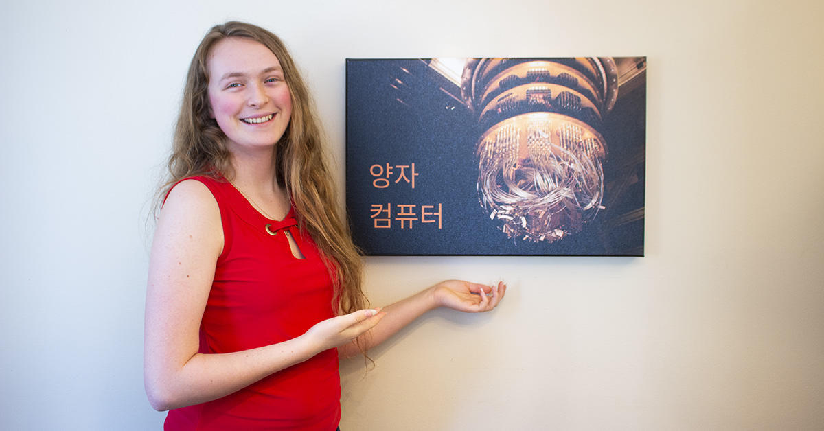 Angéline Lafleur stands next to a mounted photograph of a quantum computer.