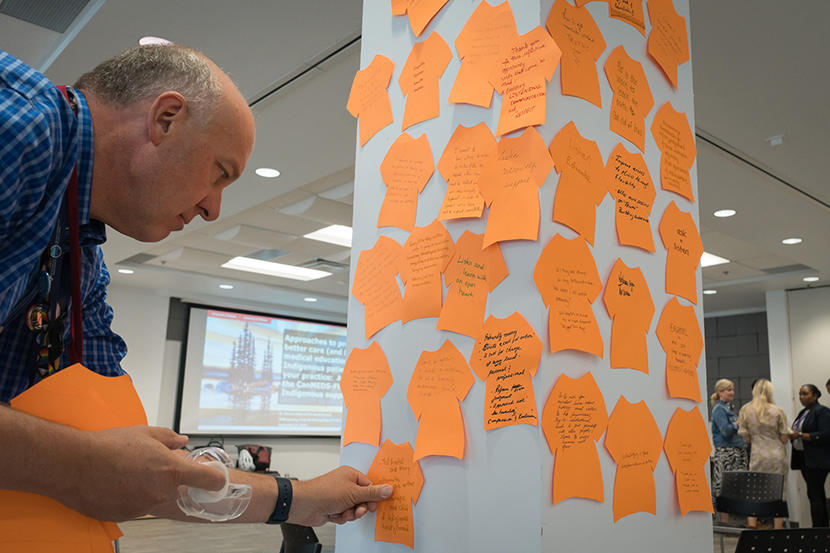 e Dr Eric Wooltorton ajoute un morceau de papier orange en forme de T-shirt sur un mur.