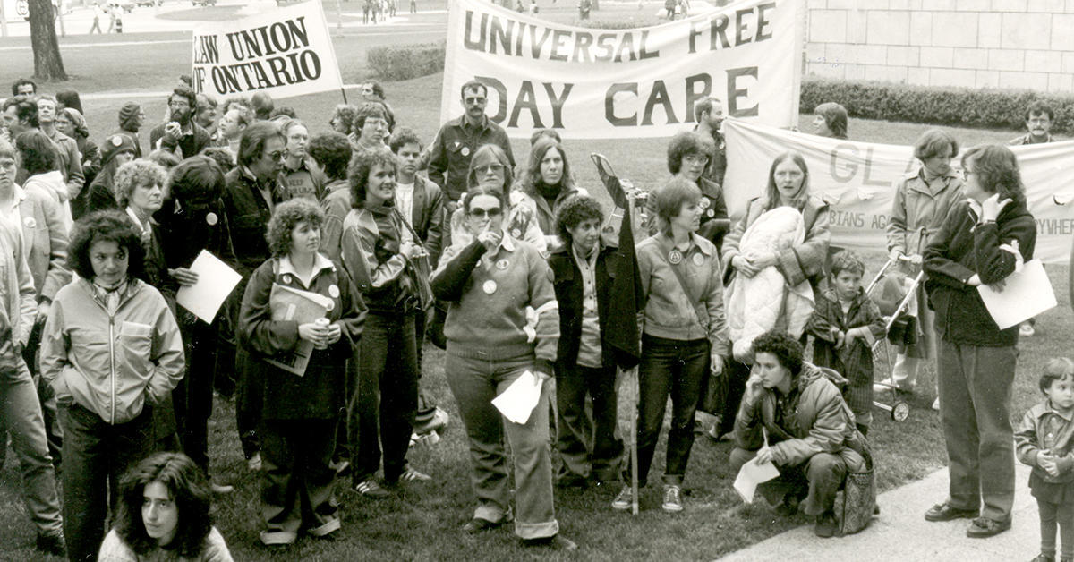 Group of women, men and children carrying a "Universal Free Day Care" banner.