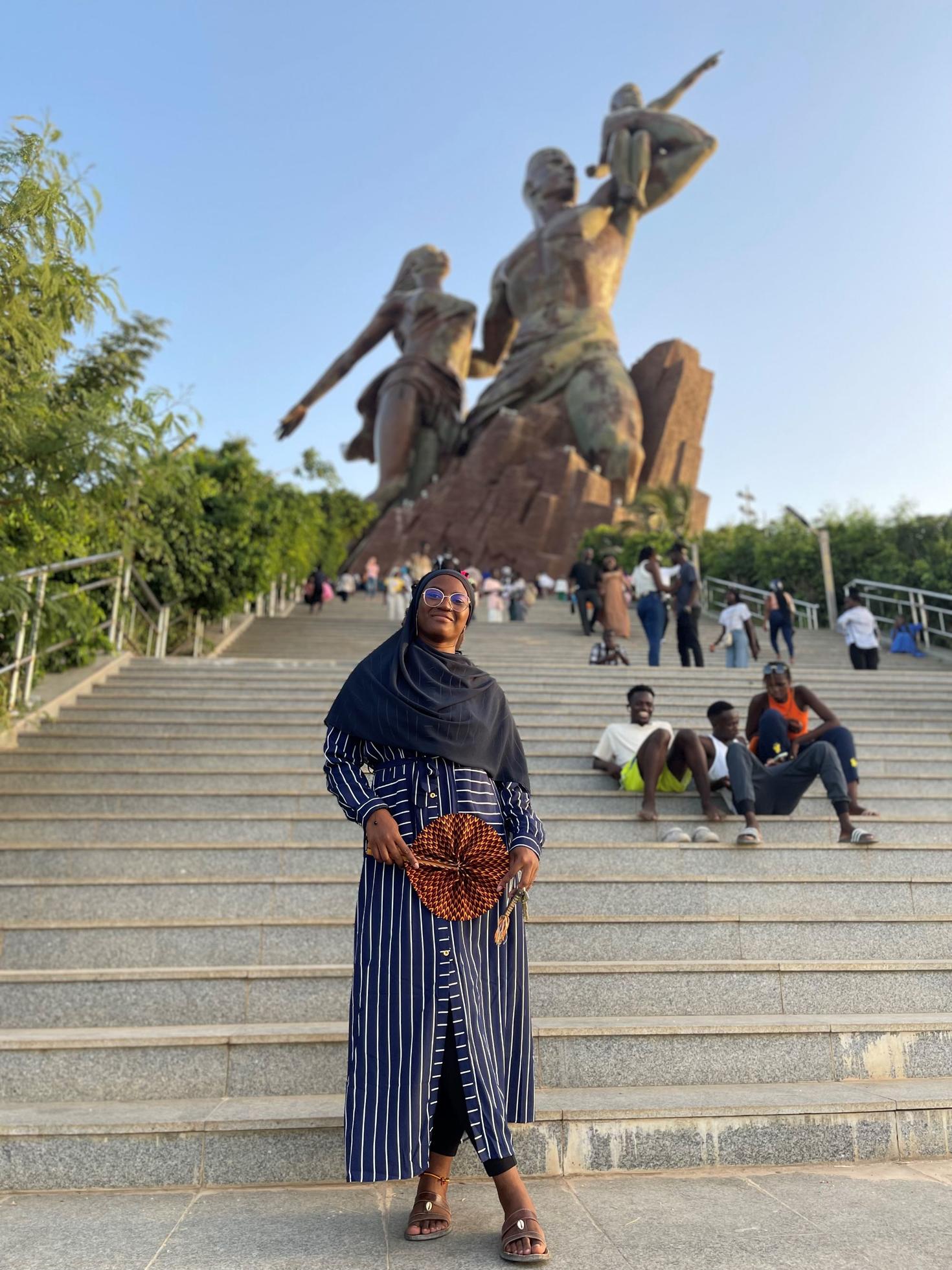 African student posing in front of steps with two tall sculptures and other people in the background. 